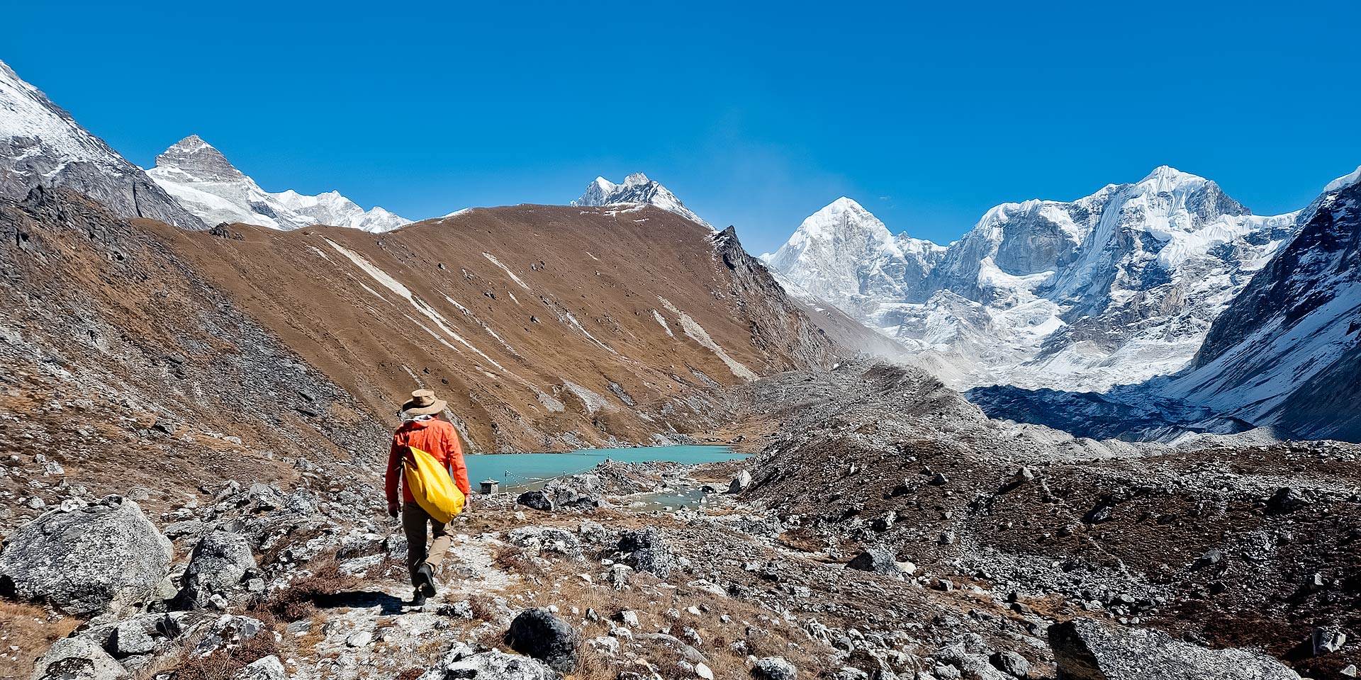 Trekker approaching Omi Tsho (Dudh Kunda) with Omi Tsho Go 6332m, Dinguing Ri, Khang Kharpo 6646m and Tragnak Ri 6801m in the background. On the Rolwaling trek in Nepal