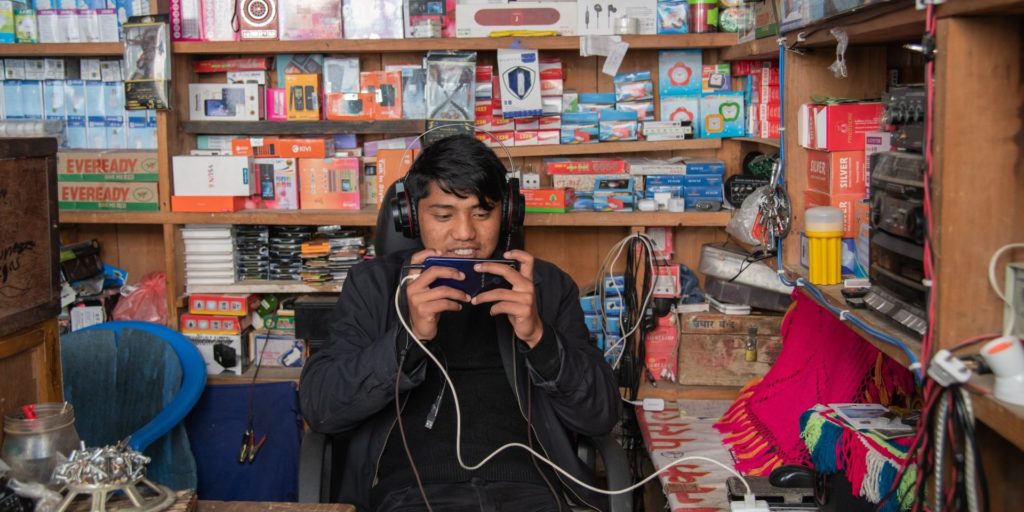 Person working in an electronics shop, wearing headphones and watching his phone.